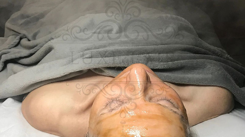 Client lying back with a warm gold facial mask applied to the face