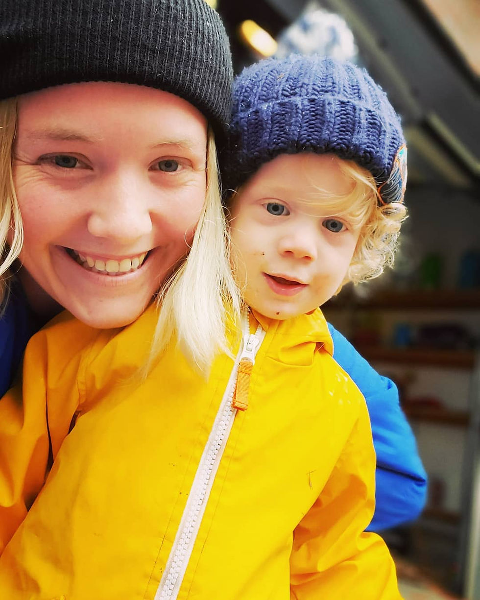 Reagan and Rowen Smile at the camera. Reagan has a black hat and blonde hair falling on either side of her face. Rowen has a navy hat and yellow rain jacket. 