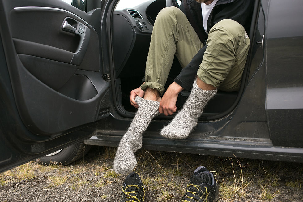 Adult puts on grey wool socks in front seat of car with green pants and black jacket