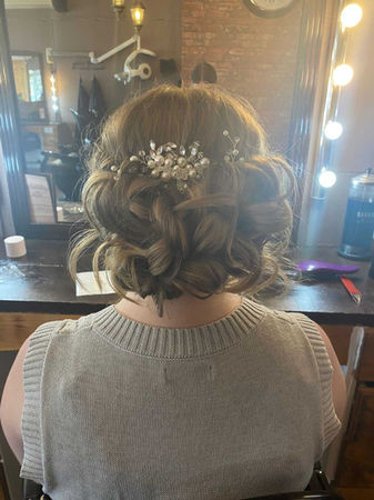 View from behind of girl sat in hairdresser with short, brown, curled hair and decorative pin