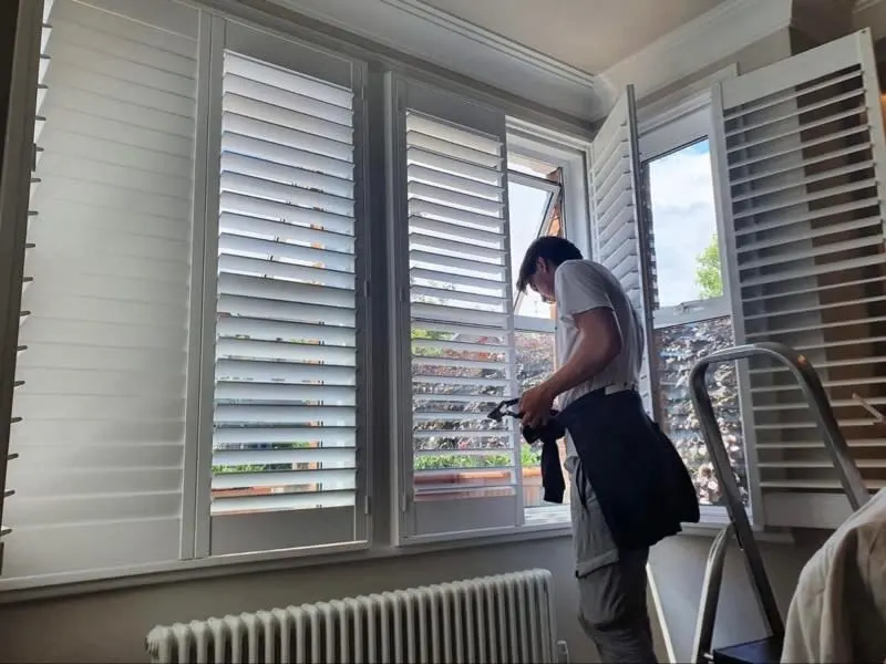 House interior, man putting up white window shutters