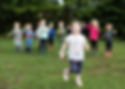 Gorup of children stood posing for a picture outside with one child running towards the camera