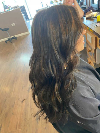 Side view of girl sat in hairdressers with long, curled, dark brown hair 