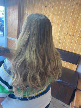 View from behind of girl sat in hairdressers with long, balayage, brown and blonde hair. 
