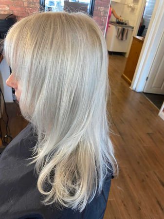 Side view of women sat in hairdressers with bleach blonde hair cut