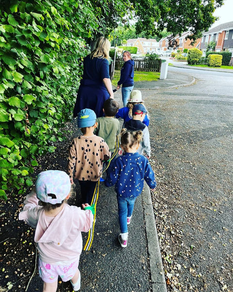 Group of children on a walk holding onto a rope with teacher at the front