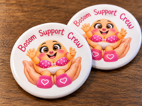 Two round white Bosom Support Crew pins featuring pink lettering and a smiling cartoon breast character wearing a polka-dot bra, photographed on a wooden surface.