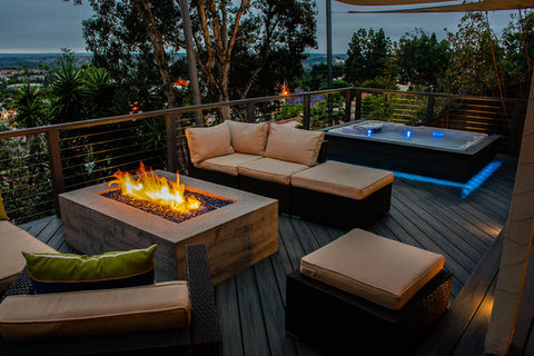Entertainment area in backyard with large deck, custom fire place made of concrete, built in Hot tub Spa Jacuzzi with outdoor lighting and seating lounge area