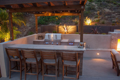 Outdoor kitchen with BBQ island with seating and covered patio above.  Stainless Grill and Cook top, outdoor lighting
