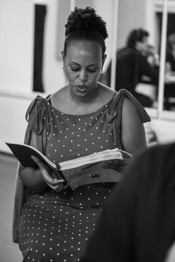 Black and white portrait of ensemble actor Geraldine sitting and looking down at her open sheet music binder.