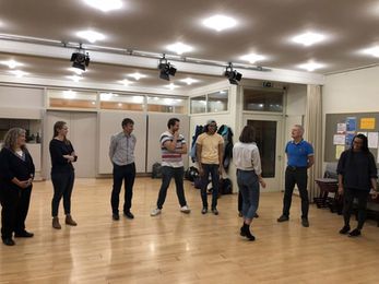 A diverse group of participants standing in a circle, warming up with an improv exercise.