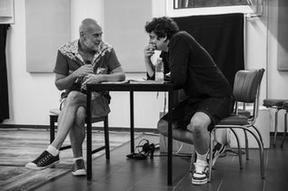 Ensemble actor Tony speaks with co-director Lucian at a table during a ZEST rehearsal for the musical RENT.