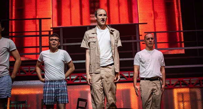 Dogfight the musical by ZEST, November 2024. Three men on stage with a red-lit set, center man in "Martin" uniform.