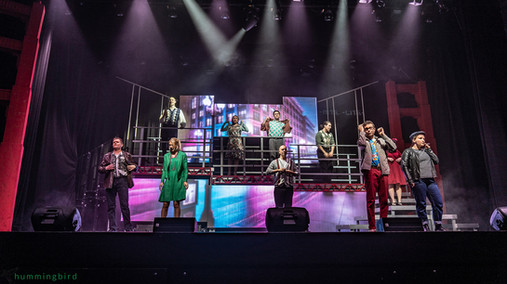 ZEST performers on a multi-level stage with a vibrant cityscape backdrop for Dogfight the musical, November 2024.