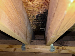 Attic roof sheathing with dark staining from past water intrusion, showing evidence of a previous roof leak around rafters.”
