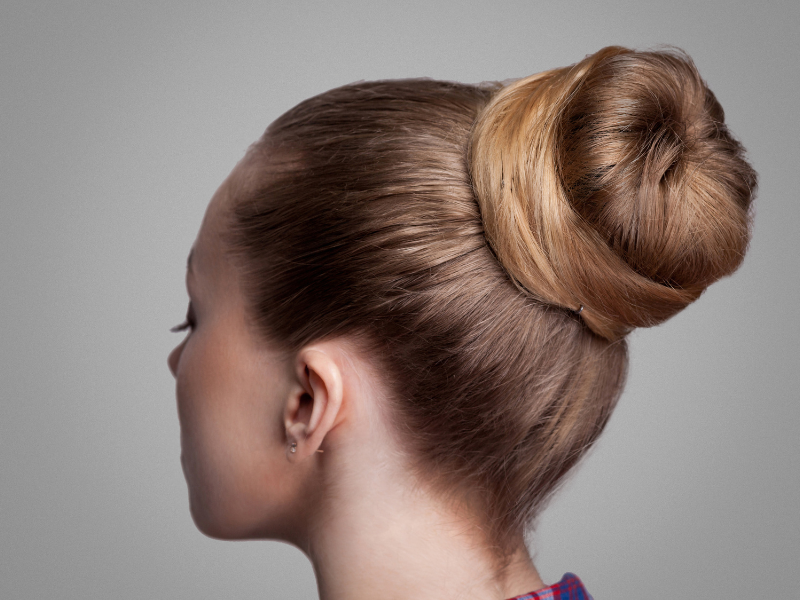 The back of a womans head wearing a tight bun in her hair.