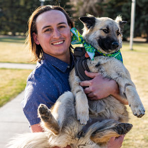 A photo of a young man smiling at the camera while holding his dog in his arms.