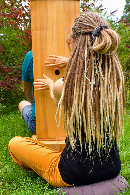 Person sitzt auf dem Klangstuhl, der von der Therapeutin im Grünen bespielt wird