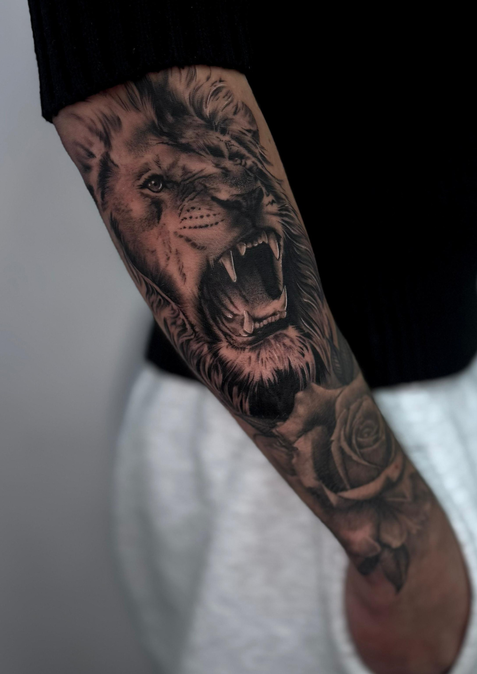 Detailliertes Tattoo eines brüllenden Löwenkopfes auf einem Arm.