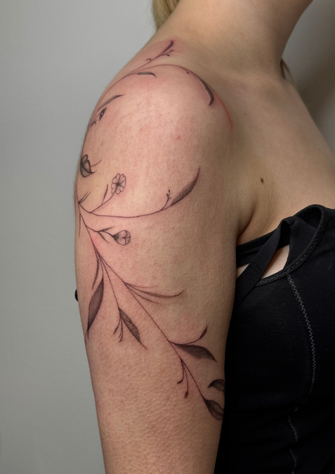 Filigranes Ranken-Tattoo auf der Schulter und dem Oberarm einer Frau.