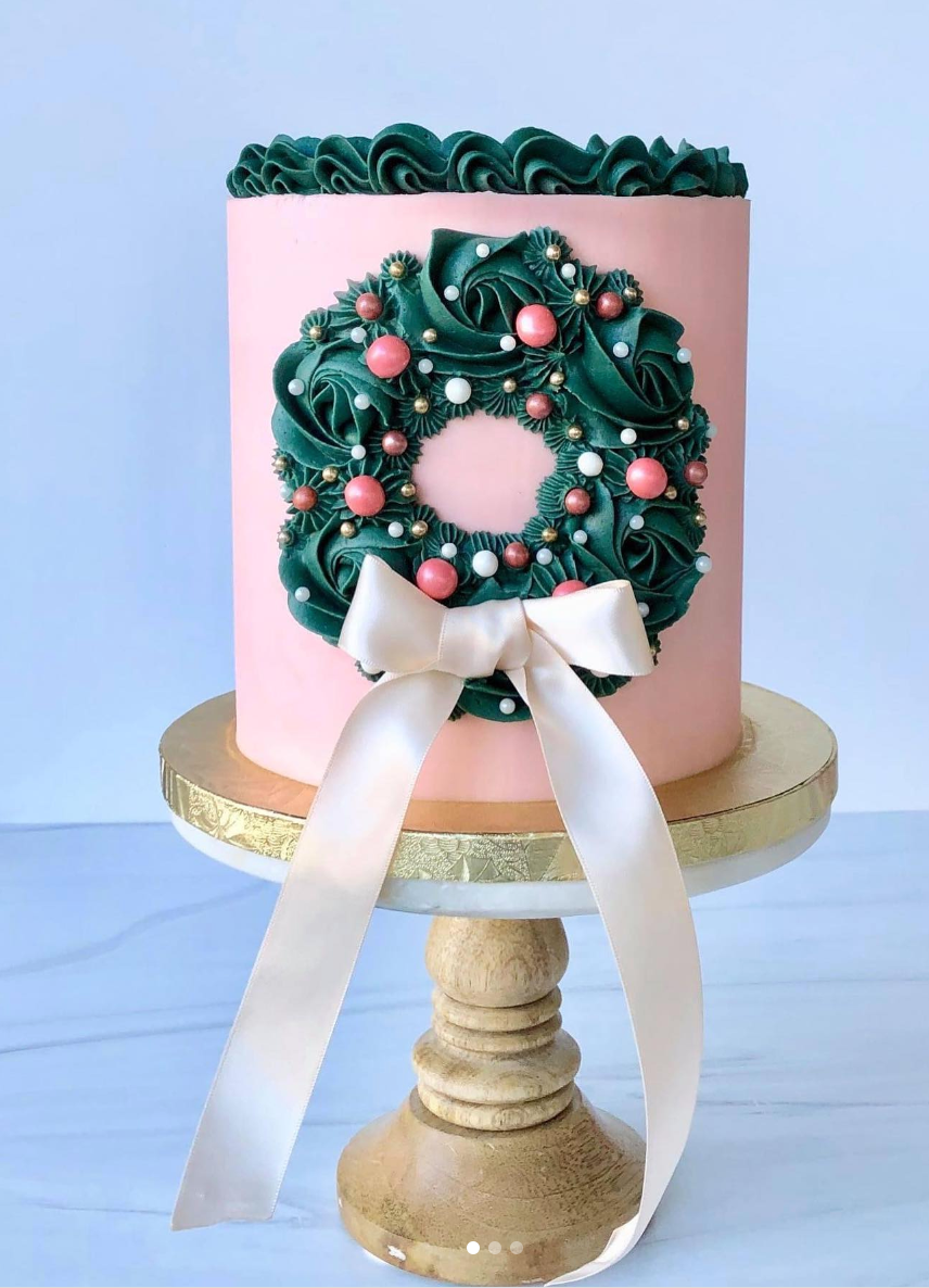 Pink buttercream cake with teal green wreath design, silk ribbon bow and edible baubles