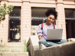 a young woman at college sitting outside with her laptop