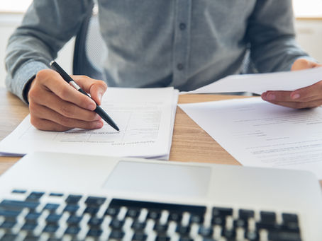 businessman sitting at table holding ballpoint pen and papers and checking documents in office
