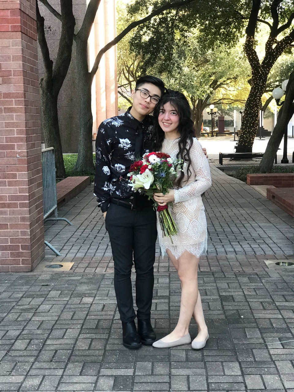 couple in casual dressy clothing standing on sidewalk holding bouquet