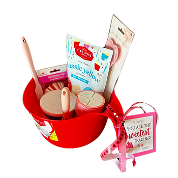 A gift basket put together for Valentine's Day. It is for cupcake ingredient bowls containing cake mix, frosting, spatula, whisk, cupcake liners, heart-shaped spatula, and sprinkles. There is a gift tag and ribbon tied to the handle of the bowl.
