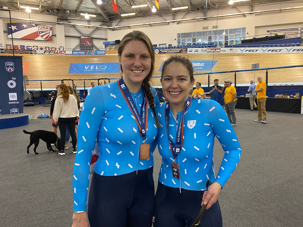 PD: Ash and Kristin at the Para Cycling Track Open. They are both smiling big and have their arms around each other. Around their necks are medals!