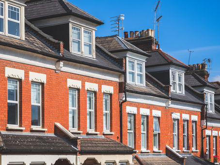 A row of red brick terrace houses with dormer loft conversions, shown against a blue sky background. No text.