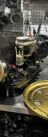 Car transmission and flywheel sit on a work bench in front of tools.