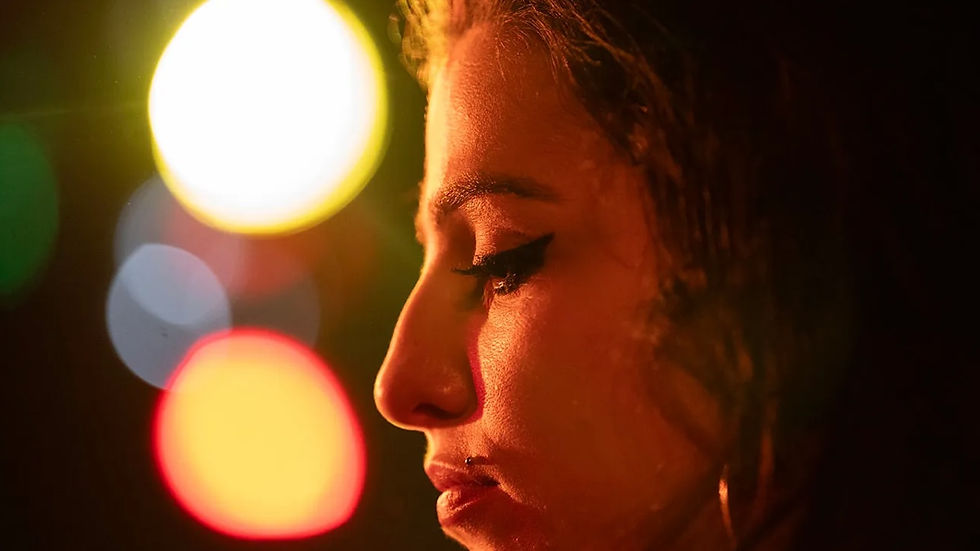 Amy Winehouse vista di profilo nel film Back to Black e in sfondo delle luci di scena sfocate