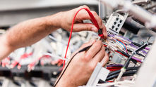 Hands testing electrical wiring inside a machine