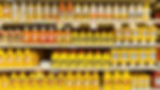 Grocery store shelves filled with assorted mustard bottles in yellow packaging, including Heinz. Price tags visible below. Bright and organized.