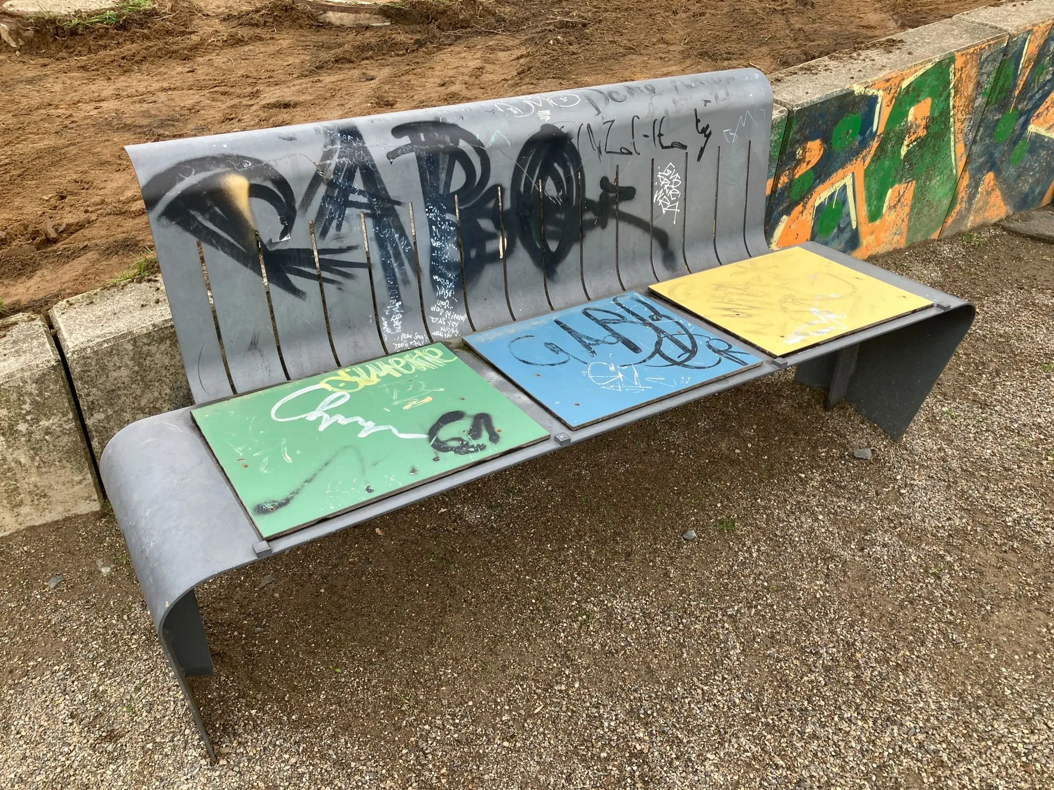 Graffitientfernung Zukunftsgarten Duisburg: Metallbank mit übereinandergelegten Graffiti-Tags vor der Reinigung