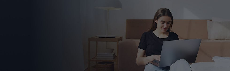 Étudiante devant son ordinateur. Elle est assise dans son salon au bas de son canapé.