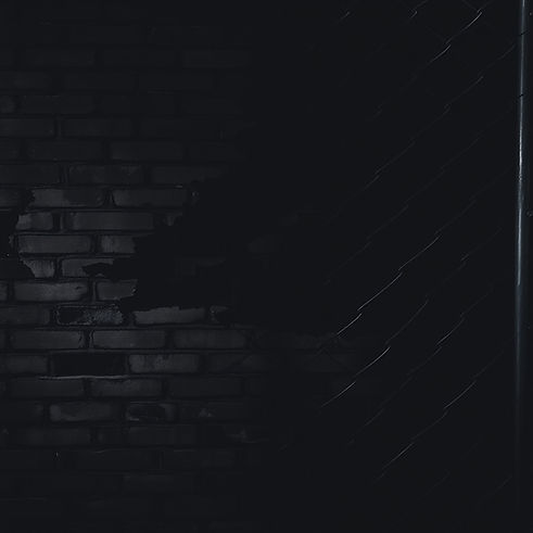 A dark, moody background featuring a weathered brick wall partially overlaid with chainlin