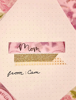 A homemade card for Mom with cut-and-pasted floral accents, a calligraphies address to "mom", and two pieces of gold washi tape for decoration.