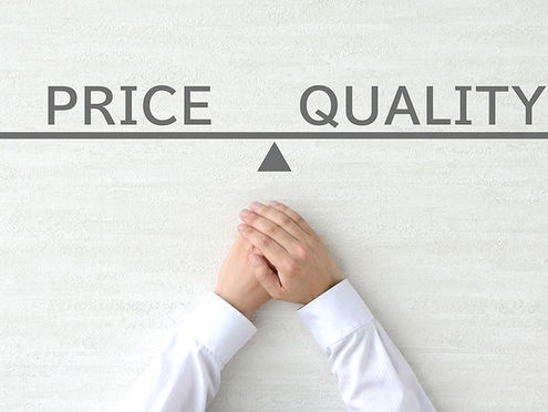 A person's hands resting below a drawn balance scale showing the words Price and Quality perfectly balanced on a white background, representing the relationship between cost and value.
