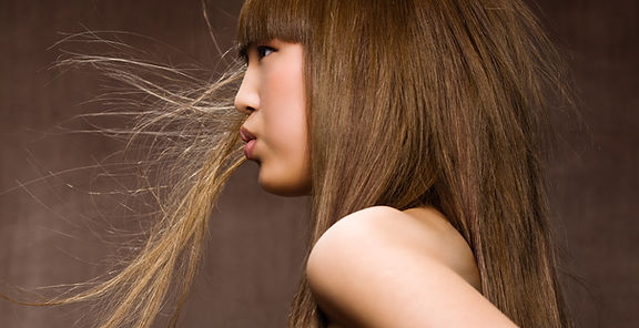 Asian woman with long brown hair blowing in the wind, low-maintenance hair coloring.