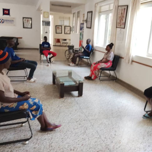Five people sitting in a reception area with a white tile floor and white walls with pictures in Uganda.