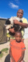 Man holds a black-and-white dog and stands behind a boy in South Africa.