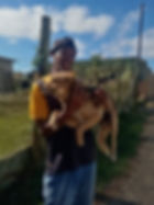 Man smiles while holding a tan and black dog in front of a house in South Africa. 