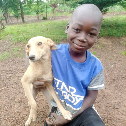 Young boy holding a tan dog and smiling in Liberia.