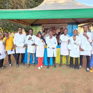 A group of students in white lab coats holding certificats under a green tent in Tanzania.
