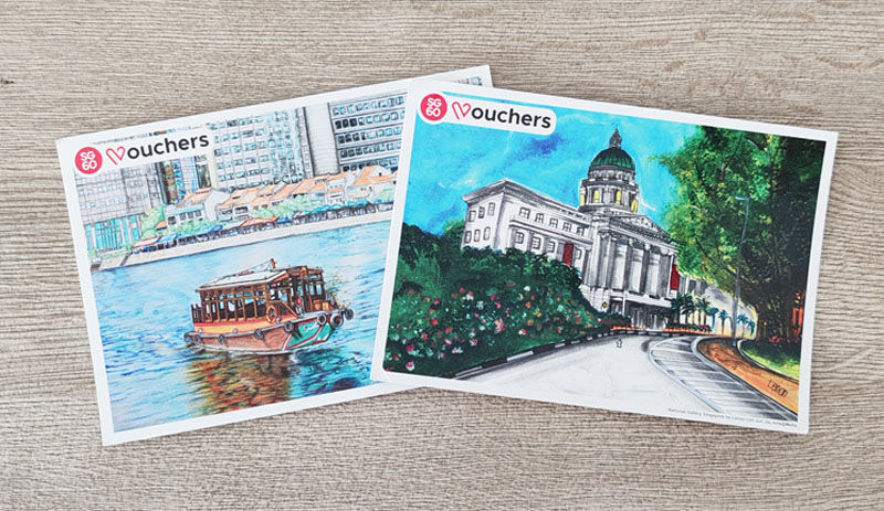 Two colorfully illustrated vouchers featuring a boat on a river and a domed building in lush surroundings, placed on a wooden surface.