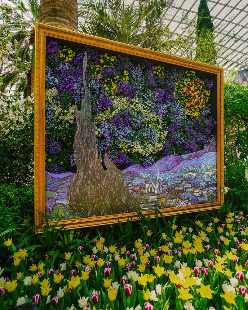 A vibrant floral arrangement recreates Van Gogh's "Starry Night" in a golden frame, surrounded by lush greenery and colorful flowers.
