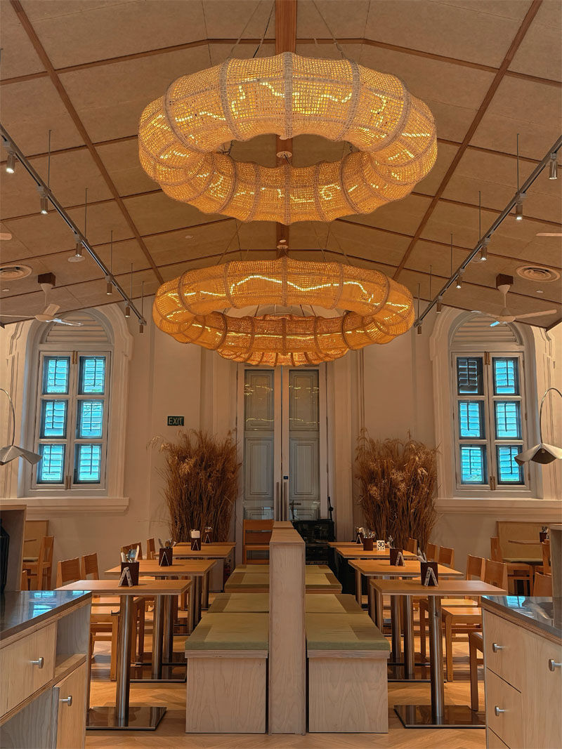 Cozy restaurant interior with warm, circular hanging lights, wooden tables, and chairs. Wheat stalks decorate corners; calm ambiance.