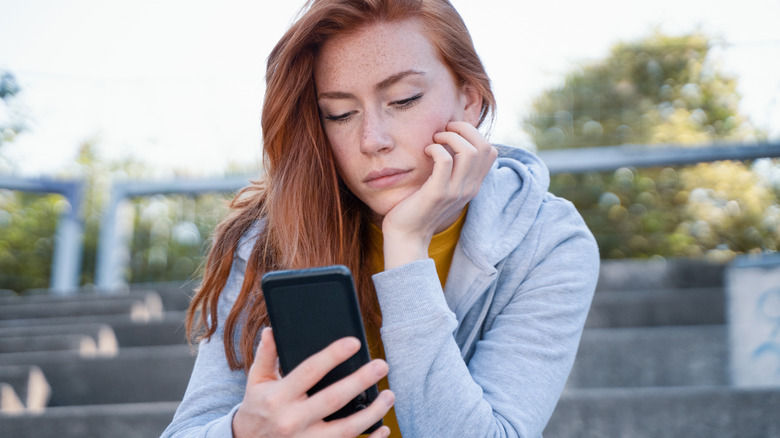woman looking forlornly at mobile device